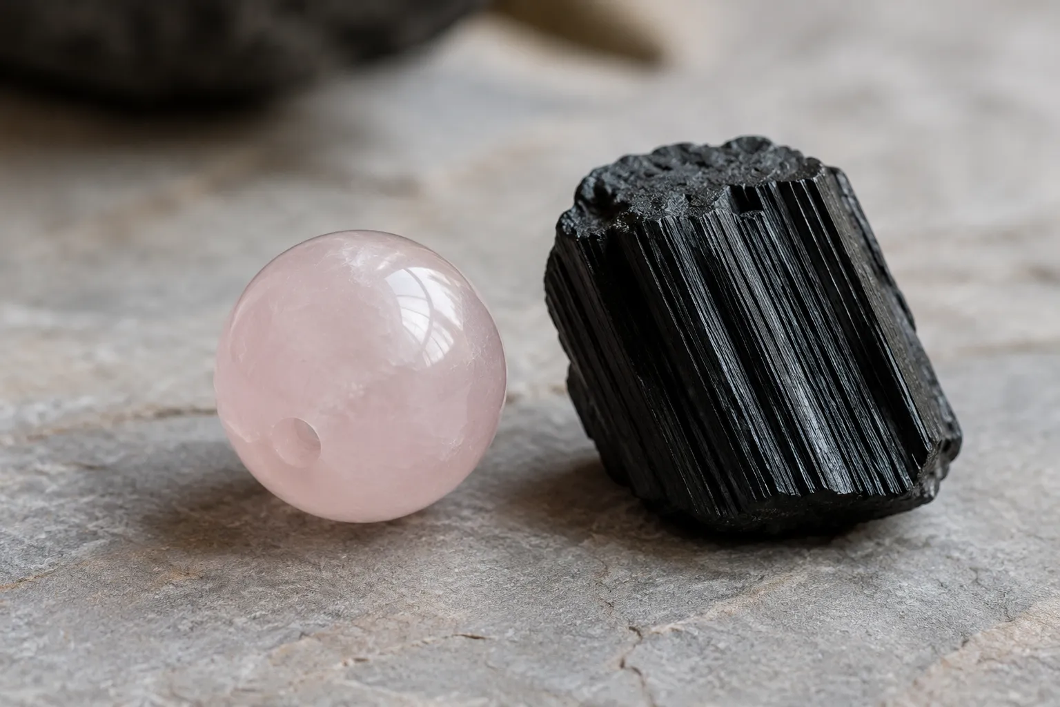 Rose quartz bead beside a dark striated black tourmaline crystal showing the pairing's visual contrast