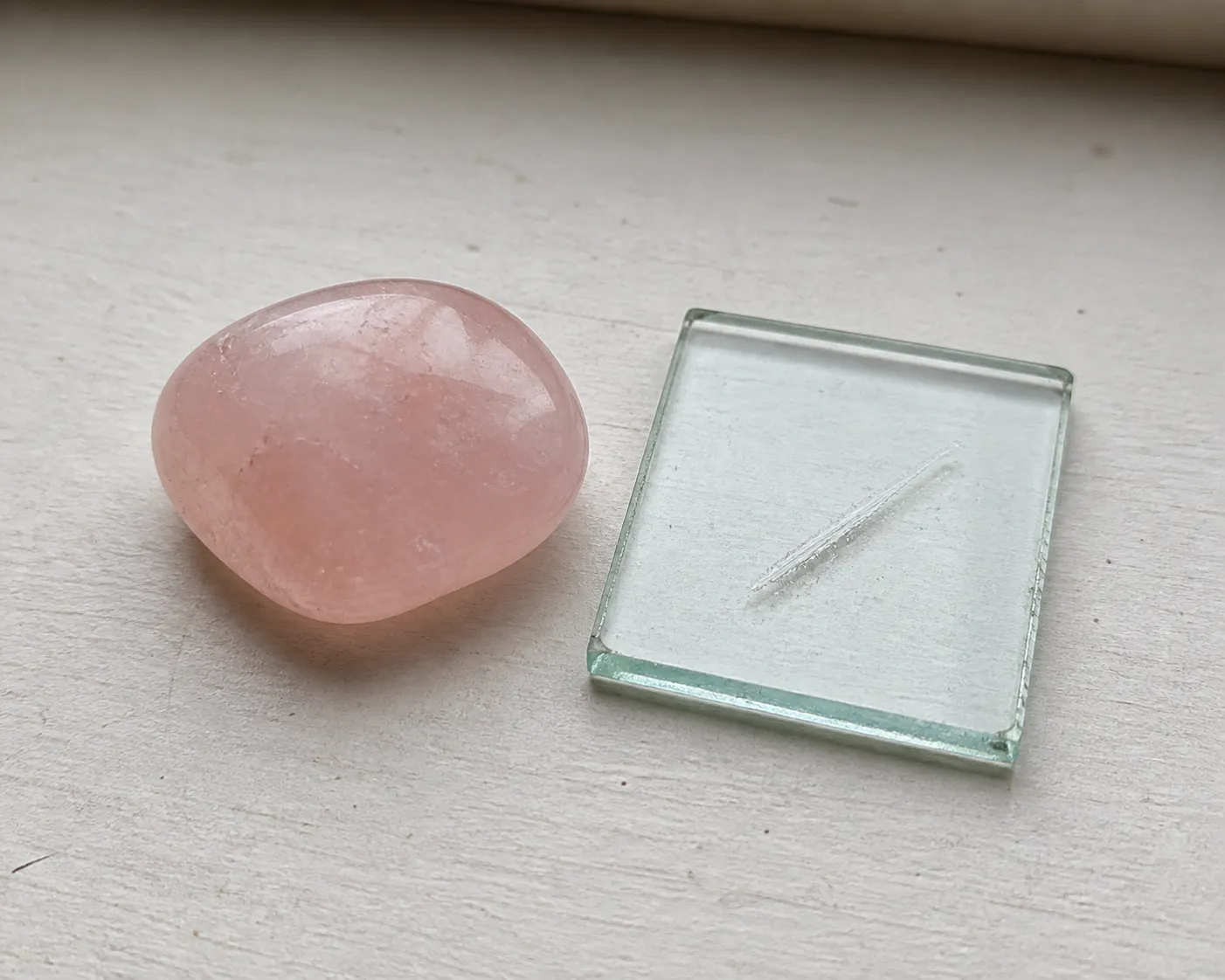 A pale pink rose quartz stone beside a glass comparison surface for a limited hardness check
